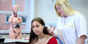 Photo of a student checking the temperature of another student with an ear thermometer